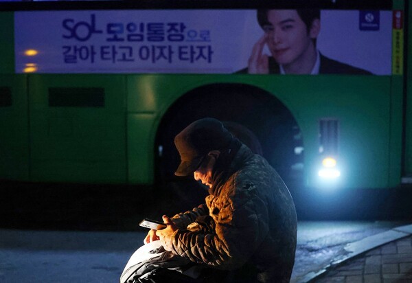지난 18일 새벽 인력사무소가 밀집한 서울 남구로역 인근에서 일감을 기다리는 일용직 구직자 뒤로 은행 광고가 붙은 버스가 지나고 있다. /사진=연합뉴스