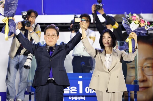 제21대 대통령 당선이 확실시되는 더불어민주당 이재명 대선 후보와 부인 김혜경 여사가 4일 서울 여의도 국회 인근에서 당 주최로 열린 국민개표방송 행사에 참석해 꽃다발을 받고서 시민들을 향해 두 팔을 들어올려 인사하고 있다. / 사진=연합뉴스